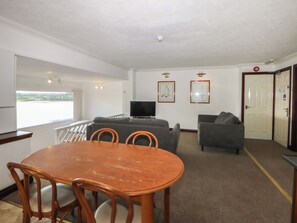 A room with a dining table, chairs, a sofa, a television, and framed pictures on the wall. - Seaview Apartment 5 (Y Felinheli)