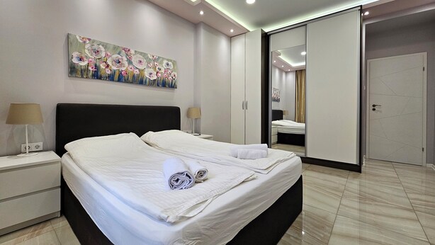 A modern bedroom with a large bed, bedside tables, a painting, and a sliding door leading to another room. - Stylish&Beutiful
Vitosha Blvd (Sofia)