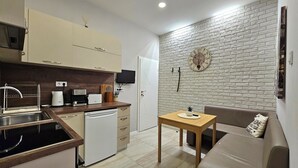 A compact kitchen with a dishwasher, a coffee maker, and a toaster. There's a small table with a plant and a clock on the wall. - Stylish&Beutiful
Vitosha Blvd (Sofia)