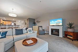 A living room with a sofa, ottoman, fireplace, television, and kitchen in the background. - 935 - Beach Days are the Best Days (Westport)