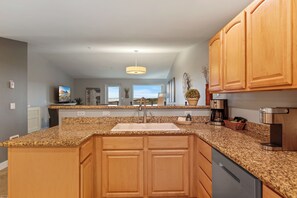 Una cocina con encimeras de granito, gabinetes de madera, pileta de acero inoxidable y una lámpara colgante.