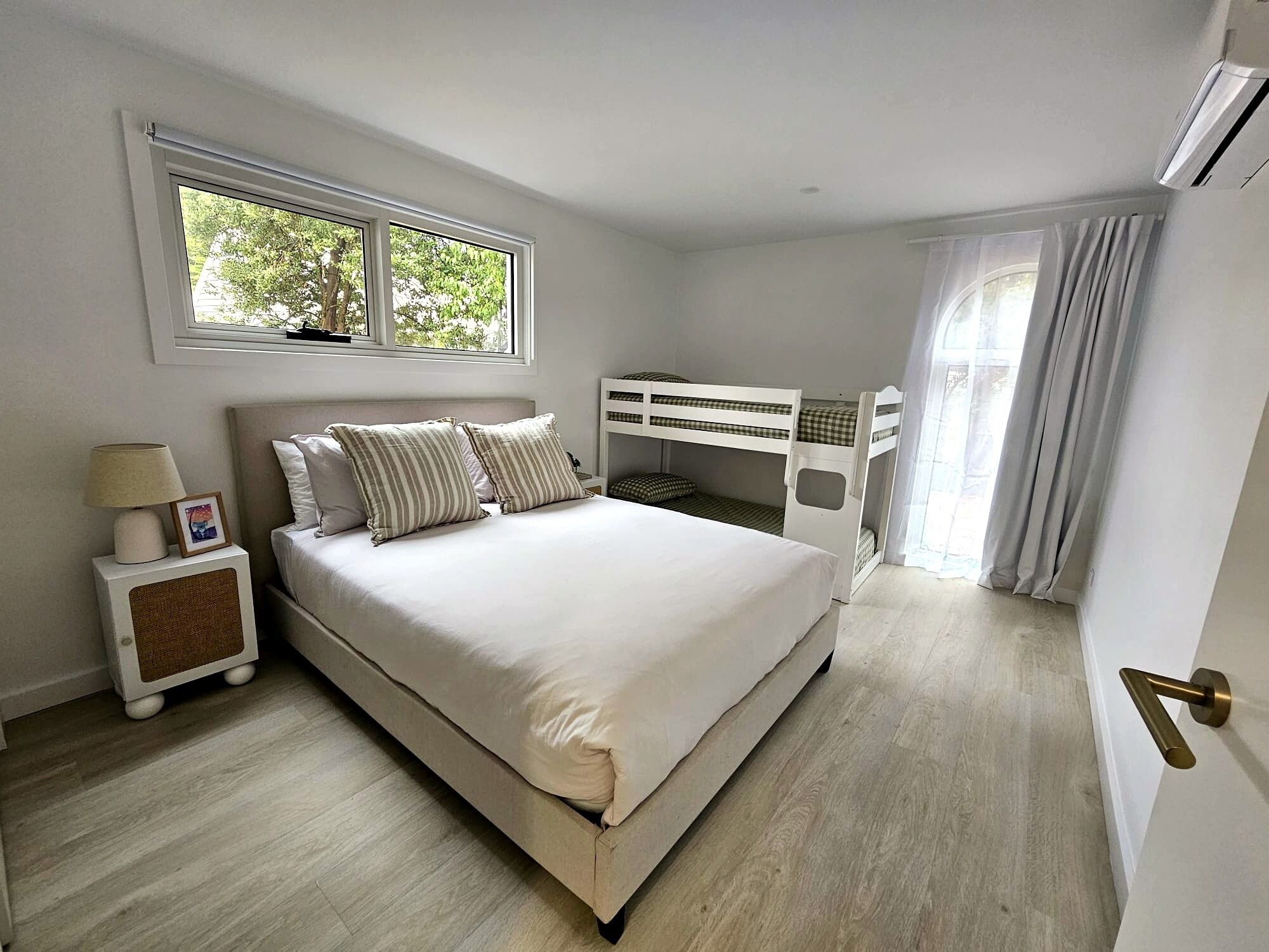 A bedroom with a bed, a nightstand, a window, bunk beds, and a door.