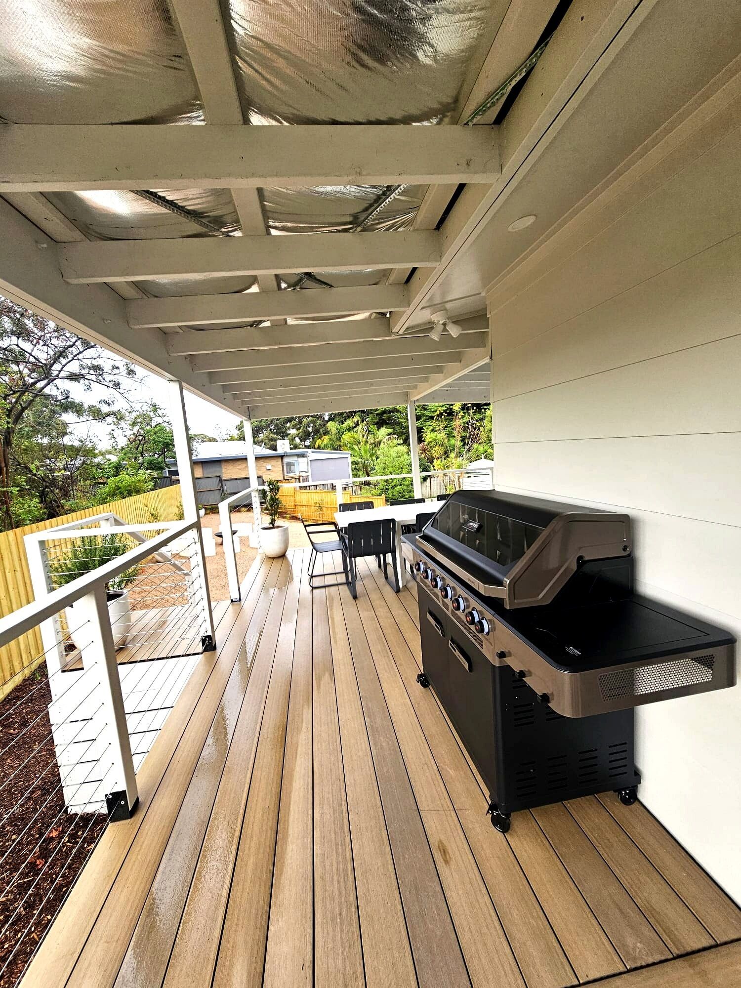 En overdækket terrasse med grill, siddepladser og udsigt over det omkringliggende landskab.