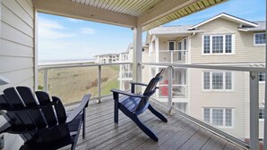 Un espace extérieur abrité doté d’une terrasse en bois, de deux fauteuils Adirondack et d’une vue sur les bâtiments en arrière-plan.