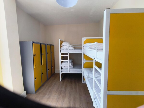 A dormitory room with bunk beds, a wardrobe, and lockers.