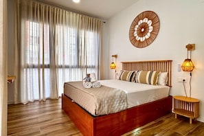 A bedroom with a wooden bed, a large window with curtains, a wall-mounted circular decoration, and two bedside lamps. - Travel Habitat Santo Domingo Loft (València)