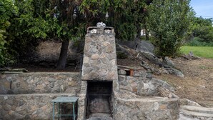 Una edificación de piedra con chimenea, una mesa de metal y escalones que la conducen.