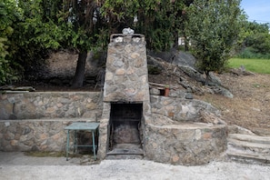 Una edificación de piedra con chimenea, una mesa de metal y escalones que la conducen.