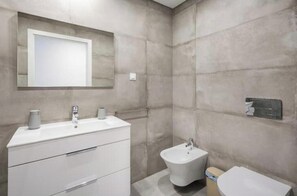 Ein modernes Badezimmer mit einem großen Spiegel, einem weißen Waschtisch, einem Bidet und einer Toilette.