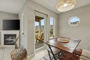 A room with a TV, fireplace, dining table, wicker chair, and a view of a building through a window. - 213 - Deepwater Digs the Go-To OceanFront Escape (Westport)