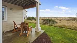 Una casa con porche cubierto, dos sillas de madera y vista a un campo de césped.