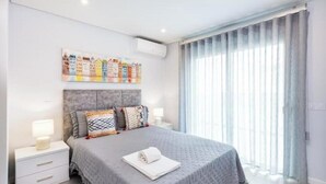 Un dormitorio con cama, mesitas de noche, aire acondicionado de pared y una ventana con cortinas.