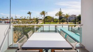 Un balcón con mesa y sillas, con vista a un puerto deportivo y palmeras.