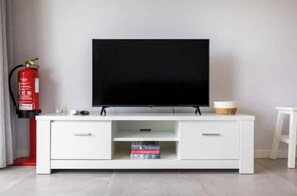 Eine weiße Unterhaltungsanlage mit Fernseher, einem Feuerlöscher und einem kleinen Tisch mit einem Korb.