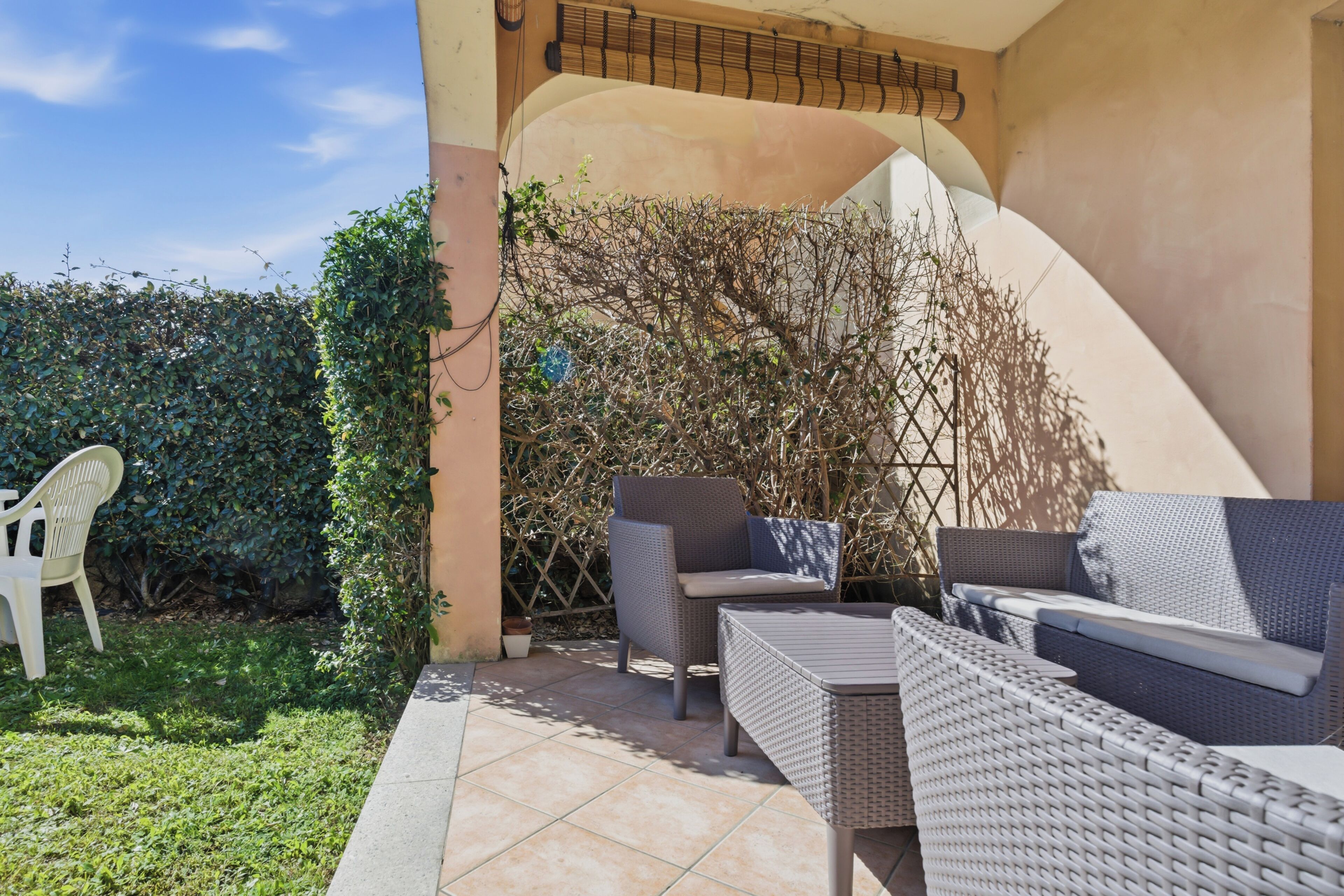 Eine Terrasse im Freien mit Korbmöbeln, einem weißen Kunststoffstuhl und einer Wand mit geschwungenem Design.