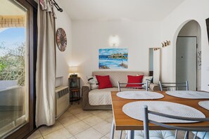 A room with a dining table, chairs, a sofa with red cushions, a painting on the wall, and a view through a window. - Cozy house Murta Maria (Murta Maria)
