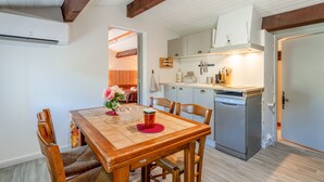 Ein Essbereich mit Holztisch und -stühlen, eine Küche mit Geschirrspüler und eine Decke mit freiliegenden Balken.
