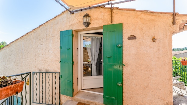 Ein Gebäudeeingang mit Tür, grünen Fensterläden, einem Metallgitter und einer Fußmatte.