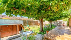 Eine Terrasse mit Tisch und Stühlen, eine Holzterrasse und ein Baum, der Schatten spendet.