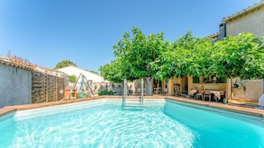 Ein Schwimmbecken mit klarem Wasser, umgeben von einer Terrasse mit Gartenmöbeln und einem Baum.