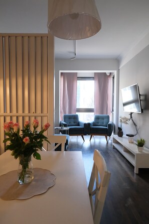 A modern living room with a dining table, two chairs, a TV mounted on the wall, and a large window with curtains. - Garbary Residence I Old Town (Poznań)