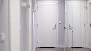 Valoisa käytävä, jonka seinät ovat valkoiset, lattia on puuta ja siinä on lasiseinä.