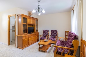 Una sala de estar con un aparador de madera, dos sillones estampados, una mesa de centro y un televisor.