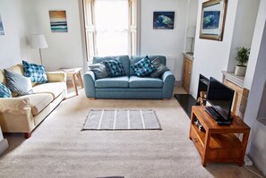 Una sala de estar con un sofá azul, un sofá beige, un mueble de televisión de madera y un tapete a rayas.