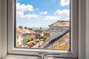 Vista por la ventana a una calle con edificios, cielo despejado y un candado en el marco.