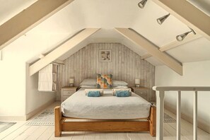 A bedroom with a sloped ceiling, a wooden bed frame, two bedside tables, and a small window.