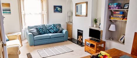 Una sala de estar con un sofá azul, una mesa de centro de madera con fruta, una chimenea y un televisor.