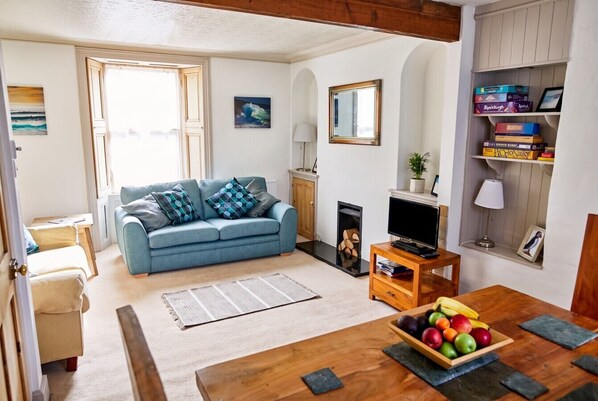 A living room with a blue sofa, a wooden coffee table with fruit, a fireplace, and a television.