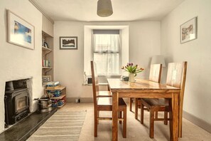 A dining area with a wooden table, chairs, a fireplace, and a window with curtains.