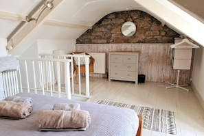A bedroom with a sloped ceiling, a stone wall, a bed with towels, a dresser, a chair, and a hanging light fixture.