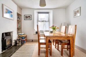 A dining area with a wooden table and chairs, a fireplace, and a window with curtains. - Character and comfort in the heart of west Cornwall (Penzance)