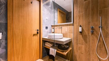 Ein modernes Badezimmer mit Holztür, einer Duschkabine aus Glas, einem weißen Waschbecken und einem Handtuchhalter.