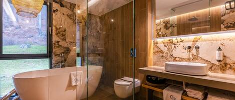 A modern bathroom with a freestanding bathtub, a toilet, and a sink with a marble backsplash.