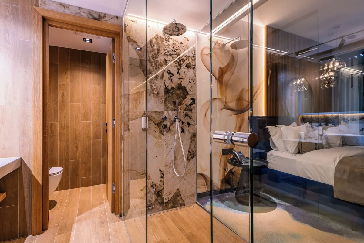 Un baño moderno con cabina de ducha de vidrio, puerta de madera y retrete a la vista.