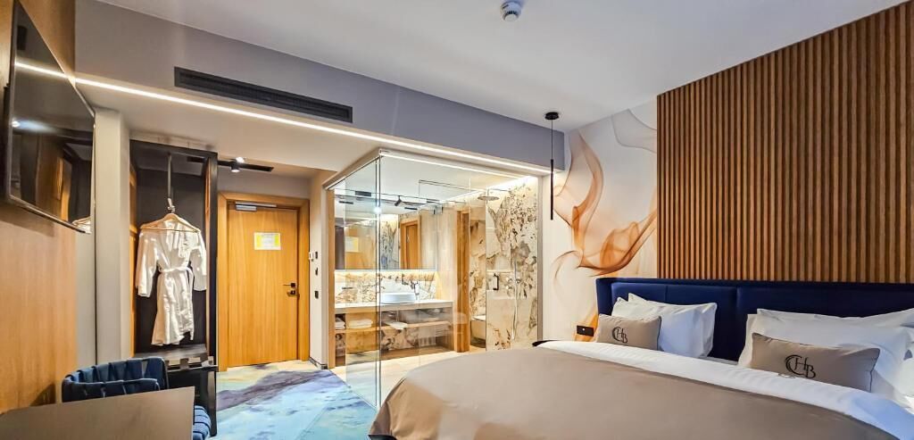 Una habitación de hotel moderna con una cama grande, un vestidor y un baño con cabina de ducha de vidrio.