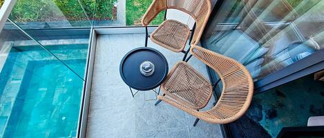 A rooftop terrace with a pool, two wicker chairs, and a table.