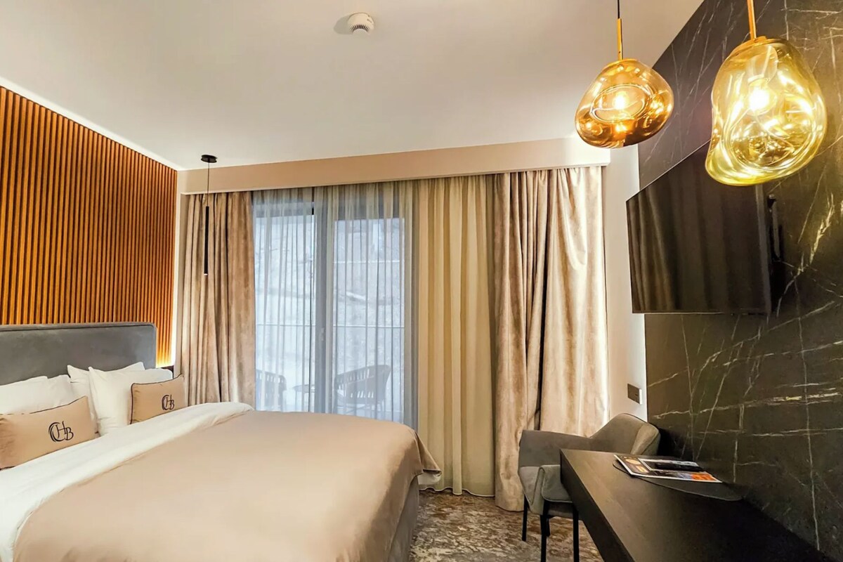 A hotel room with a bed, a desk, a chair, and a large window with curtains.