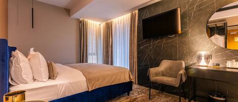A hotel room with a bed, a desk, a chair, a TV mounted on the wall, and a large mirror.