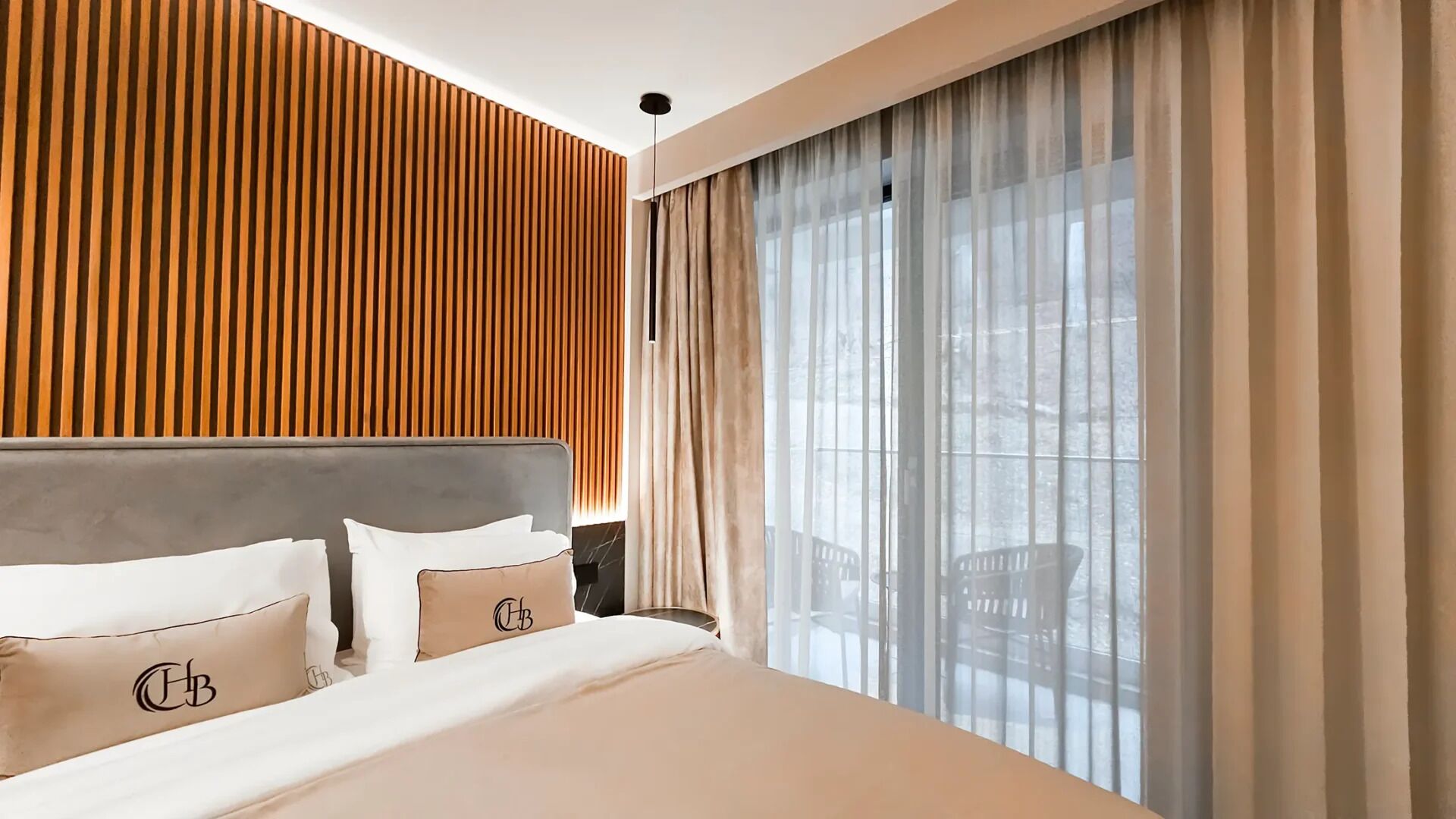 A hotel room with a bed, wooden panel wall, large window with curtains, and a view of the outdoors.