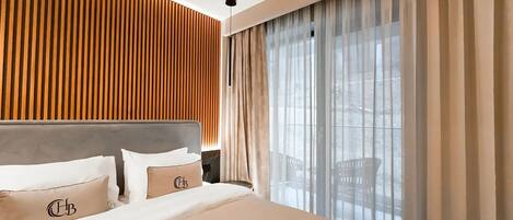 A hotel room with a bed, wooden panel wall, large window with curtains, and a view of the outdoors.