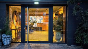 Ein moderner Gebäudeeingang mit Glastüren, Fliesenboden und Kübelpflanzen.