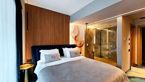 Ein modernes Hotelzimmer mit einem großen Bett, einem begehbaren Kleiderschrank und einer Duschkabine aus Glas.