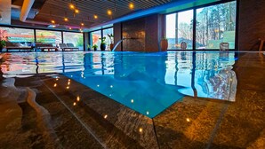 Ein Hallenbad mit klarem Wasser, Steinböden und Blick ins Freie.