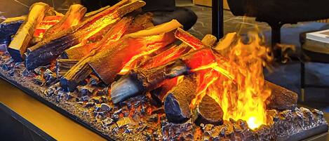Una chimenea con leña y brasas, un sofá de cuero negro y una pared divisoria de vidrio.