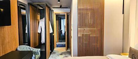 A modern hotel room with a bed, a desk, a chair, a TV, and a wardrobe.