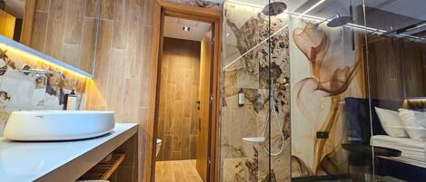 Un baño moderno con un espejo grande, un lavabo redondo, cabina de ducha de vidrio y puerta de madera.
